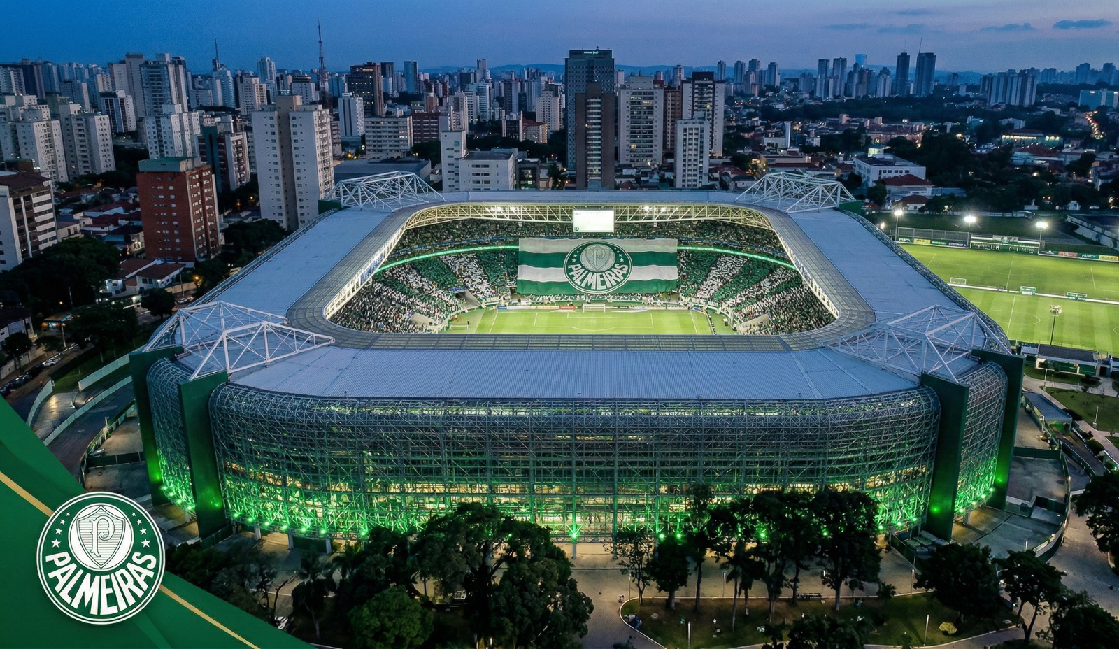 Vista aérea noturna do Allianz Parque iluminado com bandeira do Palmeiras na arquibancada